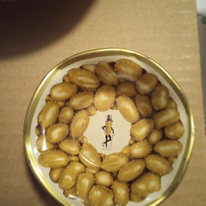 May include: A round, white, metal dish with a gold rim. The dish is decorated with a pattern of peanuts and a cartoon peanut character in a top hat and cane. The text "Mr. Peanut" is printed below the character.