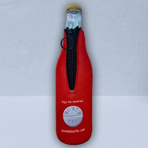May include: A red bottle koozie with a black zipper and a black ring pull. The koozie has the text "Enjoy the memories!" and a graphic of a pill with the text "RORER 714" and the website "quaaludebottle.com".