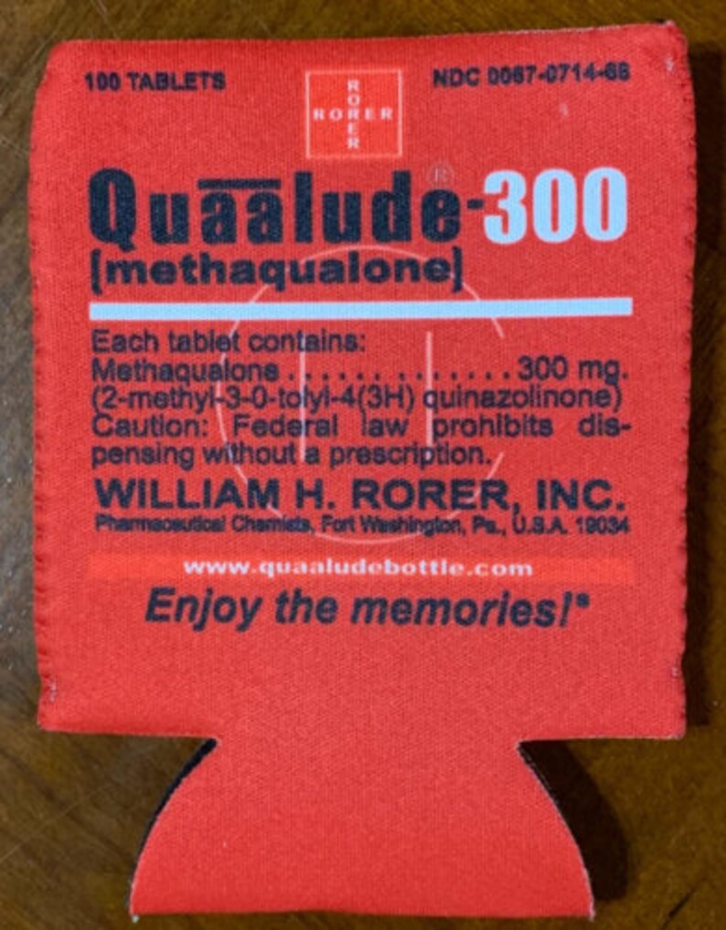 May include: A red fabric beverage insulator with the text "Quaalude-300" and "Enjoy the memories!" printed in white and black. The insulator also includes pharmaceutical information and the website www.quaaludebottle.com.