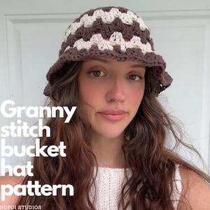 Pode incluir: Um chapéu de balde de crochê marrom e branco com um padrão de ponto de avó. O chapéu é usado por uma pessoa com cabelo castanho longo.