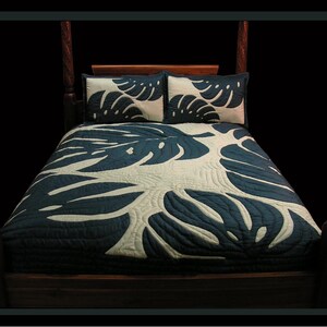 May include: A dark wood four-poster bed with a navy blue and cream-colored quilt and two matching pillow shams. The quilt and shams feature a large leaf pattern. The bed frame is dark brown.