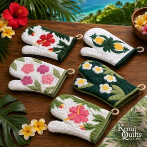 May include: Five quilted oven mitts featuring tropical floral and pineapple patterns in white, green, red, pink, and yellow. Each mitt has a hanging loop and displays embroidered hibiscus or pineapple motifs. The text Kenui Quilts EST. 2001 is visible.