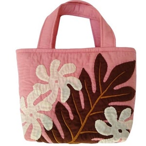 May include: A pink quilted tote bag with brown and white fabric applique leaves. The bag has two fabric handles.