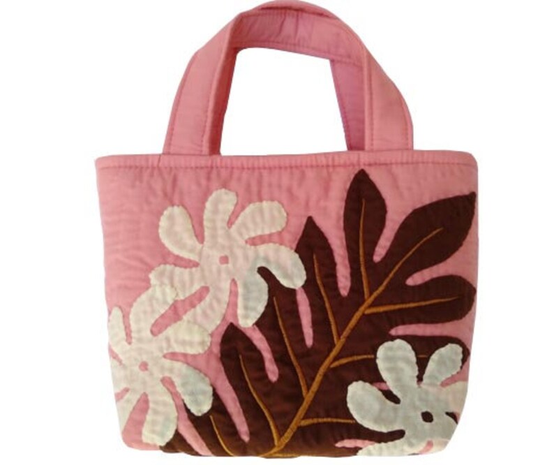 May include: A pink quilted tote bag with brown and white fabric applique leaves. The bag has two fabric handles.