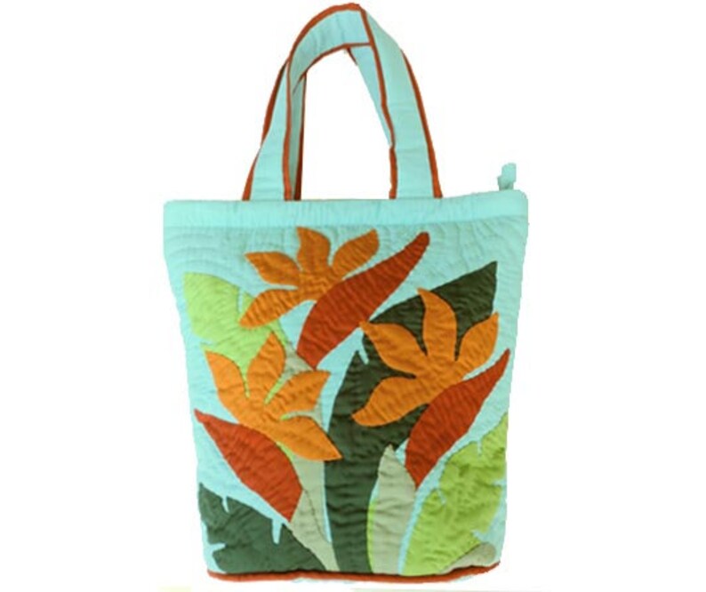 May include: A light blue quilted tote bag with orange and yellow floral applique. The bag has matching light blue handles with orange trim. The bag is approximately 12 inches wide and 14 inches tall.