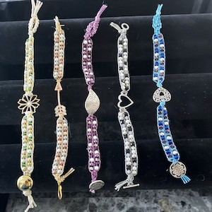 Puede incluir: Seis pulseras de cuentas coloridas con diferentes dijes. Los dijes incluyen una flor, una flecha, una hoja, un corazón y dos diseños diferentes. Las pulseras están hechas con una variedad de cuentas, incluyendo blanco, verde, morado, azul y dorado.