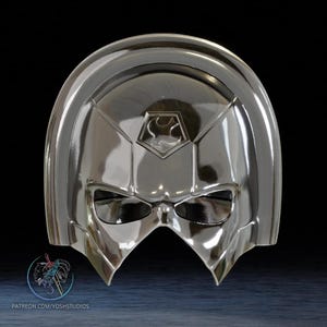 May include: A shiny, silver mask with a reflective surface. The mask features a geometric design with a central emblem and eye openings. The bottom of the mask has a pointed shape. Text at the bottom reads "PATREON.COM/YOSHSTUDIOS".