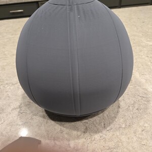 May include: A gray, egg-shaped object with vertical lines and a rounded top. The object appears to be made of a solid material and has a smooth, matte finish. The object is sitting on a speckled surface.