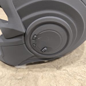 May include: Close-up of a gray, 3D-printed helmet component. The component features a series of concentric circular designs with raised details and small, rectangular protrusions. The surface has a textured appearance.