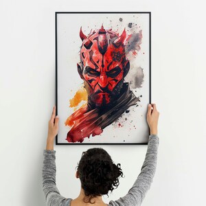 May include: A watercolour painting of Darth Maul, a character from the Star Wars franchise, with a red and black mask and horns. The painting is framed in black and is being hung on a white wall.