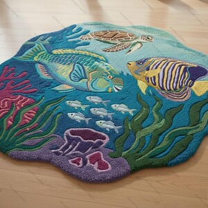 May include: A round, ocean-themed rug featuring a vibrant underwater scene. The design includes a sea turtle, colorful fish, coral, and seaweed in shades of blue, green, purple, and yellow. The rug is placed on a light-colored wooden floor.