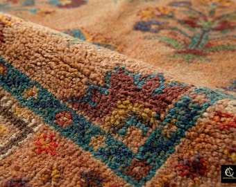 May include: Close-up of a rolled-up, intricately patterned rug. The rug features a warm, earthy color palette with detailed floral and geometric designs in shades of blue, red, yellow, and green. The texture appears soft and plush.
