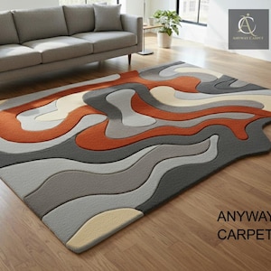 May include: A modern area rug with an abstract design. The rug features wavy patterns in shades of gray, orange, and cream. The text "ANYWAY CARPET" is visible on the rug. The rug is placed on a hardwood floor.