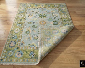 May include: A rectangular area rug with a light blue central field and a green border. The rug features floral and geometric patterns in shades of blue, green, and peach. The corner of the rug is folded up, revealing the underside.