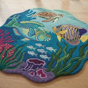 May include: A round, ocean-themed rug featuring a vibrant underwater scene. The rug depicts a parrotfish, angelfish, sea turtle, and small fish swimming among coral and seaweed. The color palette includes shades of blue, green, purple, and yellow.
