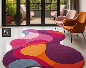 May include: A vibrant, abstract area rug with a unique, flowing shape. The rug features a bold color palette of purple, pink, orange, and blue, creating a modern and eye-catching design. The rug is placed on a white floor in a room with modern furniture.