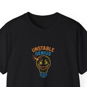 Puede incluir: Camiseta negra con un gráfico de neón de una bombilla con una cara y las palabras "UNSTABLE GENIUS" en naranja y azul. La bombilla tiene ojos "X" y una sonrisa.