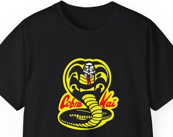 May include: Black t-shirt with a yellow Cobra Kai logo featuring a cobra with red eyes and fangs. The logo has the words "Cobra Kai" in red.