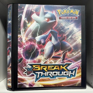 May include: A black binder with a colorful Pokemon card game image on the front. The image features a blue and purple Pokemon character with the text "Pokemon Trading Card Game" and "Breakthrough" on the front.
