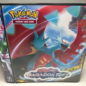 May include: A blue and red Pokemon trading card binder with the text "Pokemon Trading Card Game" and "Paradox Rift" on the front. The binder features a blue and red Pokemon with a red background.