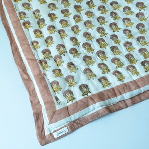 May include: A white cotton quilt with a brown and yellow floral pattern. The quilt has a brown border and a label that says "Handmade".