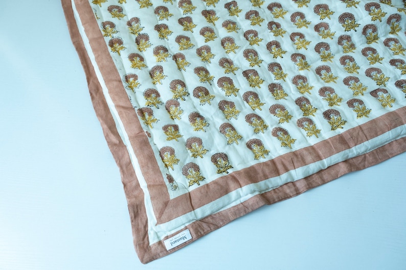 May include: A white cotton quilt with a brown and yellow floral pattern. The quilt has a brown border and a label that says "Handmade".