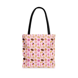 May include: A pink tote bag featuring a pattern of assorted colourful pastries and breads. The bag has black handles.