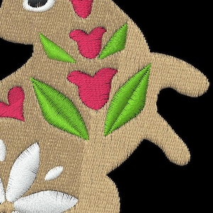 May include: Embroidered squirrel design in tan with floral and leaf accents. Features a large white flower, red hearts, and green leaves. The squirrel has a long, curved tail with green leaves. Ideal for crafts and sewing projects.
