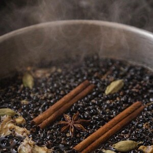 Peut inclure: Gros plan sur une casserole contenant un liquide sombre en ébullition, avec des bâtons de cannelle, de l'anis étoilé et des gousses de cardamome. De la vapeur s'élève de la casserole, suggérant une boisson chaude ou une infusion. Les ingrédients sont visibles.