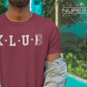 Op de afbeelding: Een maroon t-shirt met witte tekst die "K*L*U*B" zegt.
