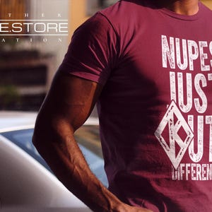 May include: A maroon t-shirt with white text that reads "NUPES JUST OUT DIFFERENT". The text is in a distressed font style.