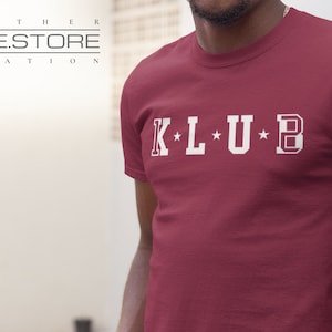 Op de afbeelding: Een maroon t-shirt met witte tekst die "K*L*U*B" zegt.