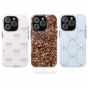 Pode incluir: Três capas de telefone com designs diferentes. Uma é branca com laços rosa, outra é castanha com manchas brancas e a terceira é azul claro xadrez vichy com laços azuis. A marca "mülkmaid" está na parte inferior.