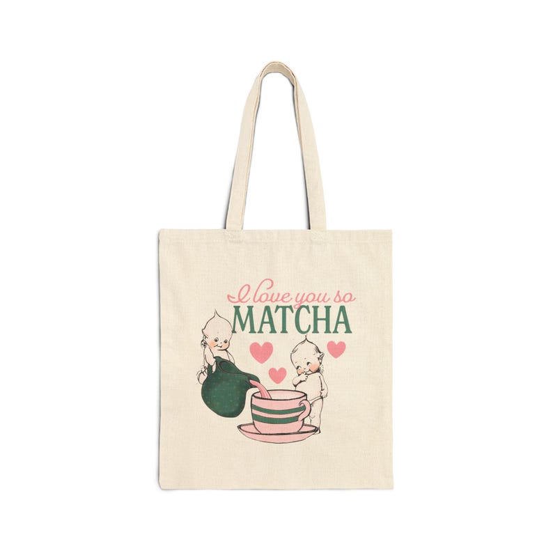 Puede incluir: Bolso tote color crema con la frase "I love you so MATCHA" y un dise&ntilde;o de dos figuras de querubines, una tetera, una taza de t&eacute; y corazones rosas. El bolso es rectangular y tiene dos asas. El dise&ntilde;o es verde y rosa.