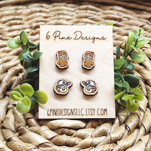 May include: Wooden stud earrings featuring cartoon characters. The earrings are displayed on a wooden card with the text "6 Pine Designs" and "6PINEDESIGNSLLC.ETSY.COM". The earrings are brown, tan, and blue.