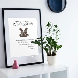 Peut inclure: Une impression d'art encadrée avec le texte The Potter et le verset biblique Isaiah 64:8, accompagnée d'une illustration graphique brune de mains façonnant de l'argile sur un tour de potier, sur fond blanc dans un cadre noir.