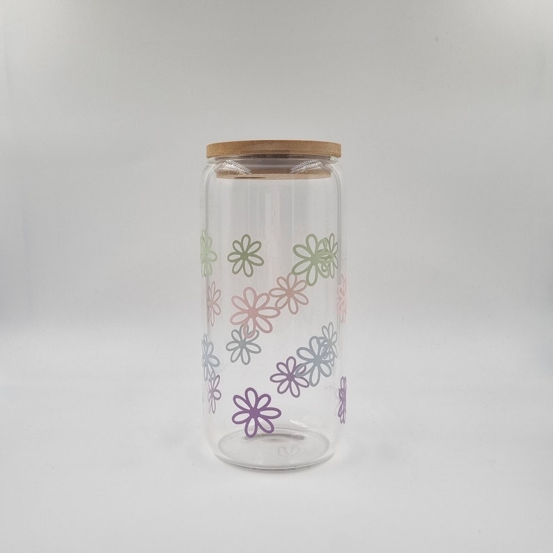 May include: A clear glass jar with a wooden lid and a floral design. The flowers are in shades of pink, green, and blue.