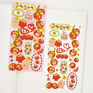 Peut inclure: Deux planches d'autocollants avec des motifs sur le thème de la tomate. Les autocollants présentent des tomates rouges avec des tiges vertes, des personnages d'ours mignons et le mot "Tomatoes". Les autocollants sont sur un fond rose.