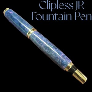 May include: A blue and purple fountain pen with gold accents. The pen is made of a marbled material and has a clip-less design.  The pen is called "Clipless JR Fountain Pen".