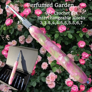 Pode incluir: Um conjunto de crochê com ganchos intercambiáveis, com uma pega marmoreada rosa e verde. O conjunto inclui nove ganchos com tamanhos que variam de 3 a 7. O texto "Perfumed Garden" é visível.