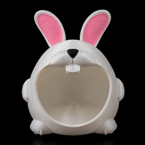 May include: White ceramic bunny-shaped Easter basket with pink ears and a black nose. The basket has a large opening for holding Easter eggs.