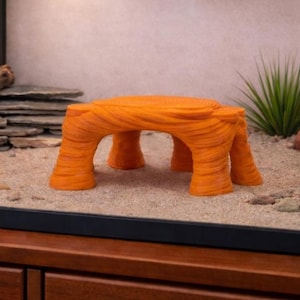 May include: An orange reptile habitat decoration resembling a miniature rock formation. The textured surface and arch-like supports create a naturalistic look. This decorative piece is designed to provide a climbing and basking spot for reptiles.