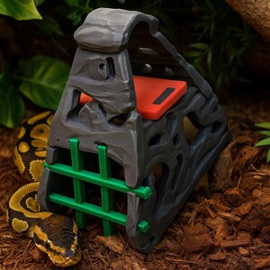 May include: A gray and black reptile hideout with a green barred front and a red top. The hideout is designed to look like a stone structure. A yellow and black snake is coiled nearby.