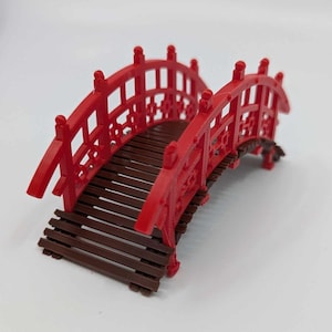 May include: A red wooden bridge with a brown wooden deck. The bridge has a traditional Japanese design with intricate details.