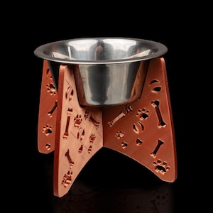 May include: A stainless steel dog bowl elevated on a wooden stand. The stand is decorated with paw prints and bone shapes and is painted a reddish-brown color.