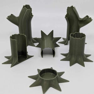 Puede incluir: Conjunto de miniaturas de tocones y piezas de árboles impresas en 3D en color verde oliva. El conjunto incluye varias secciones de troncos de árboles, algunas con ramas, y algunas bases en forma de estrella. Diseñado para juegos de mesa o maquetas.