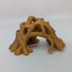 May include: A detailed, tan-colored miniature tree stump with an arched opening. The sculpture features a textured surface, mimicking the look of tree bark, and is designed with multiple openings and a rounded base.