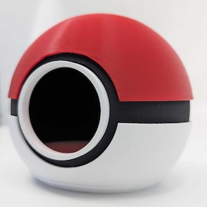 May include: A red, white, and black spherical object with a large circular opening. The top half is red, the bottom half is white, and a black band separates the two. The opening is surrounded by a white ring.