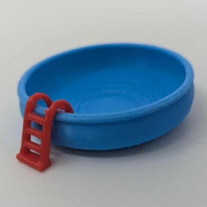 Puede incluir: Una pequeña piscina azul redonda con una escalera roja. La piscina tiene una superficie lisa y la escalera roja está unida al lateral. Esta piscina en miniatura es probablemente un juguete o un objeto decorativo.