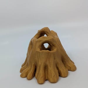May include: A 3D-printed, tan-colored tree stump with multiple openings. The stump has a textured surface and a naturalistic design, suitable for decorative purposes or as a small animal habitat.